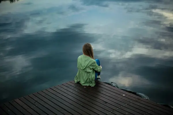 Woman sitting alone on wooden planks, looking out into water. Photo by Keenan Constance from Pexels: https://www.pexels.com/photo/woman-sitting-on-wooden-planks-2865901/